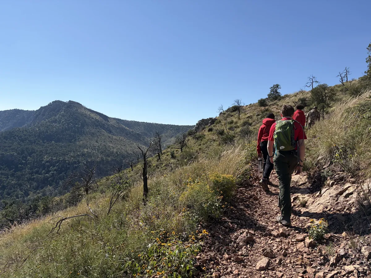Scouts follow a rocky hillside trail above a broad mountain valley.