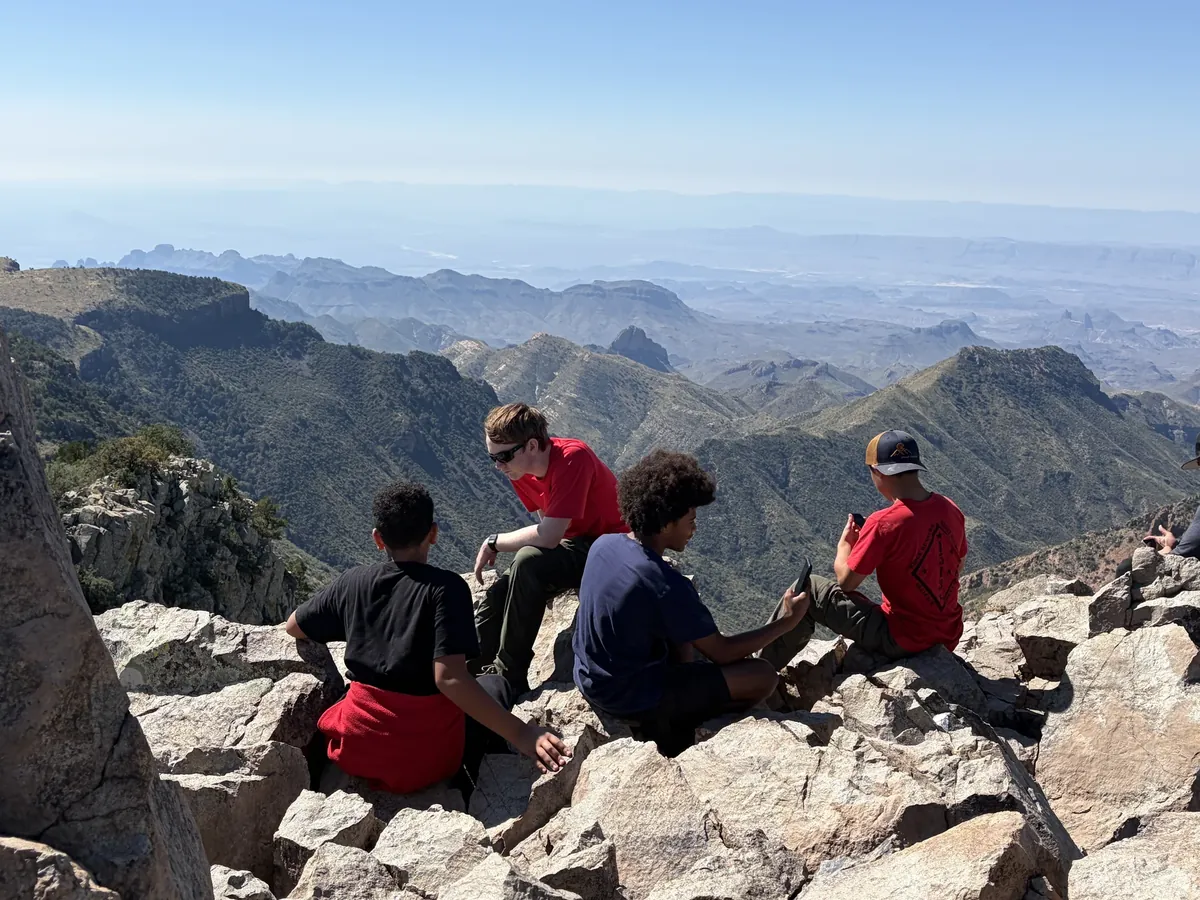 Companions sitting among rocks with layered mountains extending into the distance.