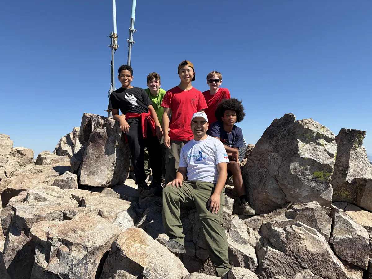 Scouts and a trip participant posing together among large rocks beneath a clear blue sky.