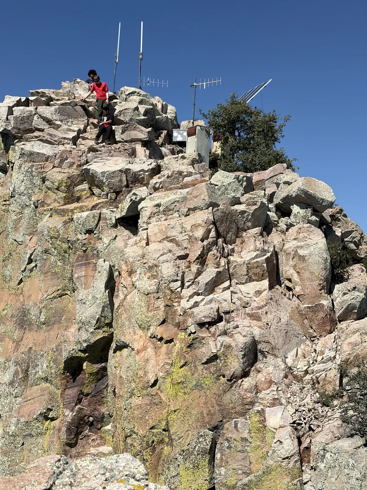 Three Scouts moving down rocky steps below antennas against a clear blue sky.