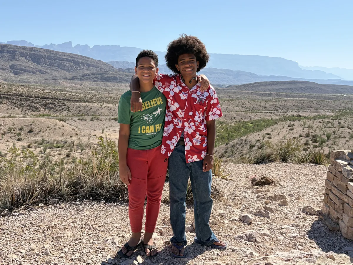 Two smiling companions standing with an arm around shoulders at a desert overlook.