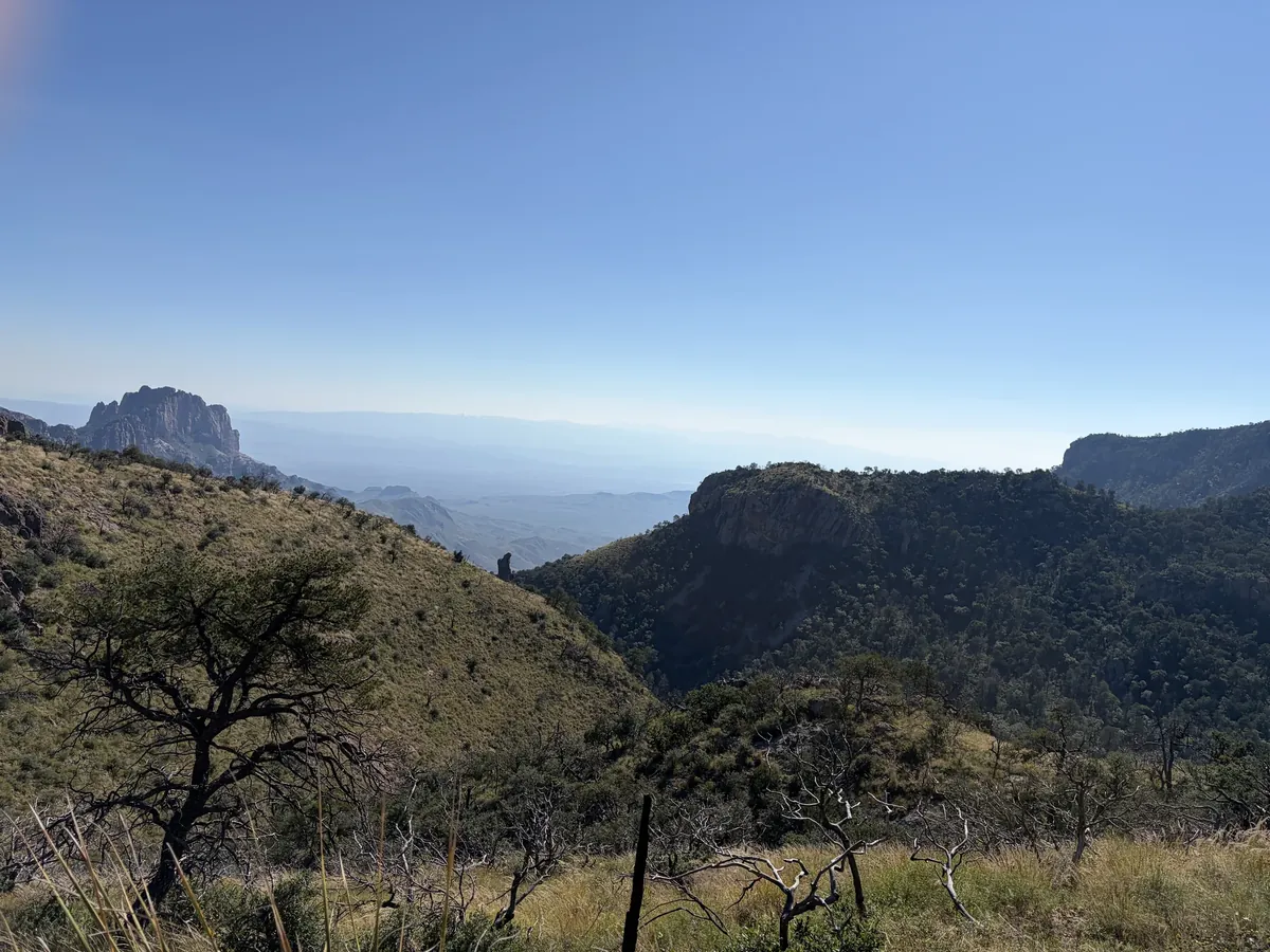 Layered mountain ridges and wooded slopes fading into the distance beneath a blue sky.