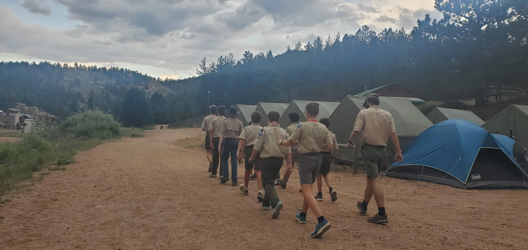 Scouts walking together through a mountain campsite lined with tents