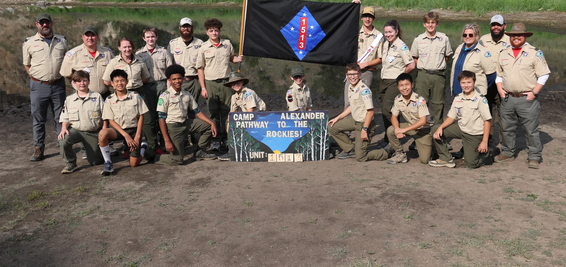 Troop 1513 Scouts and adult leaders gathered with their troop flag at summer camp