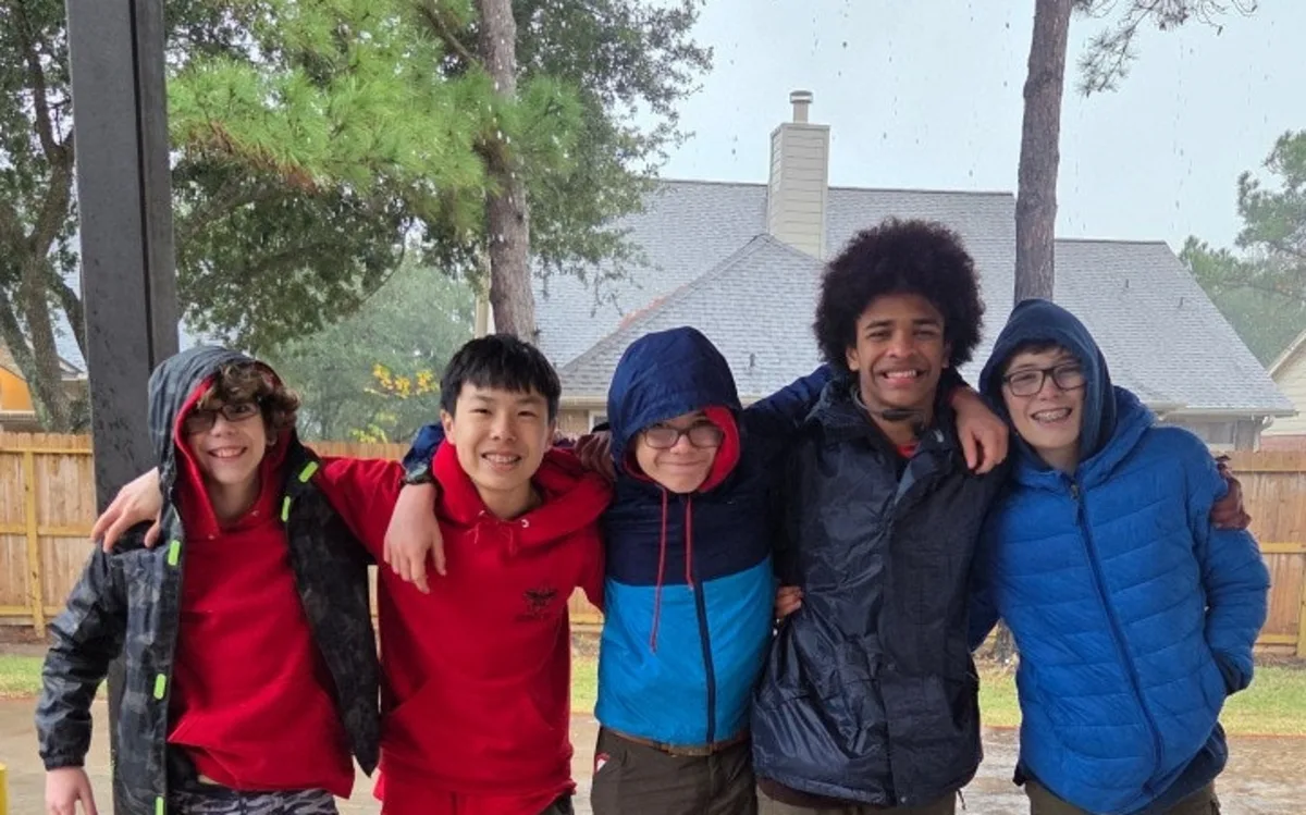 Five Troop 1513 Scouts smiling with their arms around one another after a rainy camp activity